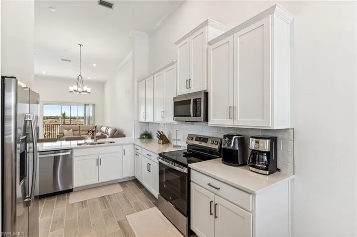 Kitchen featuring open floor plan, appliances with stainless steel finishes, white cabinetry, backsplash, and a chandelier