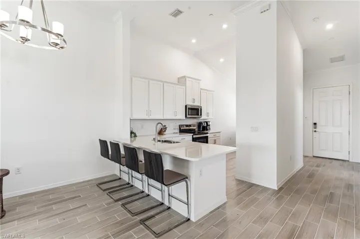 Kitchen with a kitchen bar, white cabinetry, appliances with stainless steel finishes, crown molding, and wood tiled floors