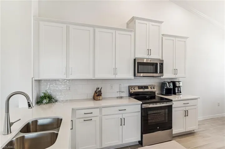 Kitchen with appliances with stainless steel finishes, white cabinets, decorative backsplash, and lofted ceiling