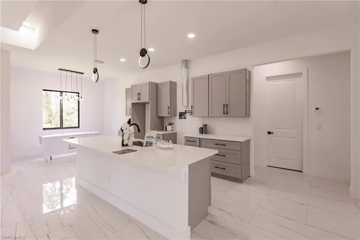 Kitchen featuring gray cabinetry, a center island with sink, pendant lighting, sink, and light tile floors