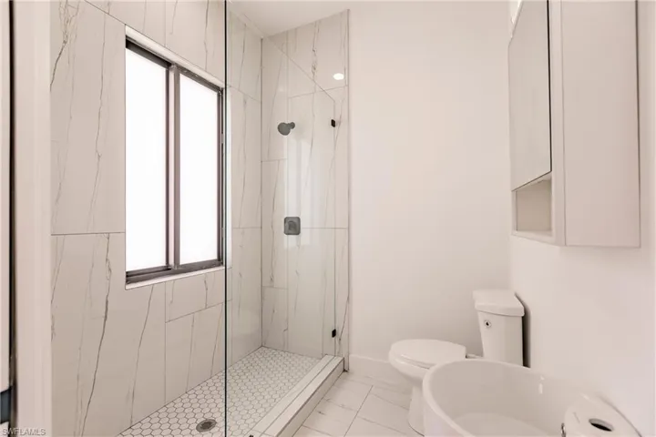 Bathroom featuring a shower with shower door, tile flooring, and toilet