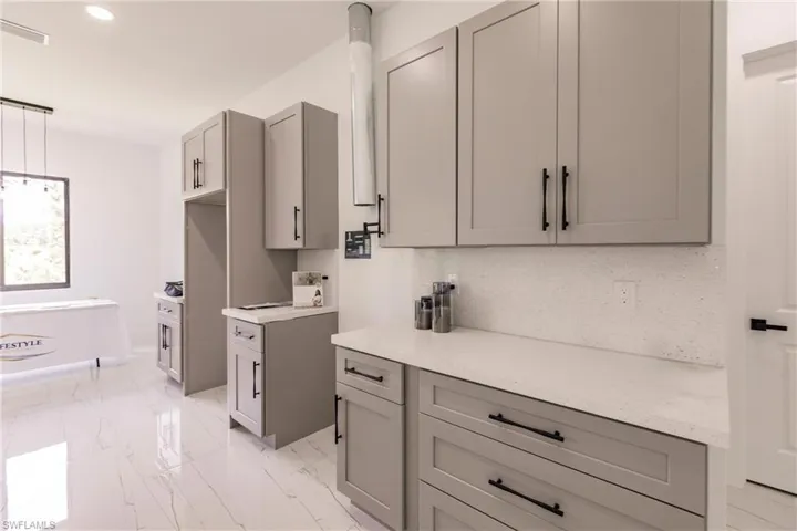 Kitchen with light stone countertops, decorative light fixtures, light tile flooring, and tasteful backsplash