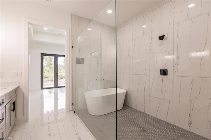 Bathroom with tile flooring, tile walls, shower with separate bathtub, and vanity