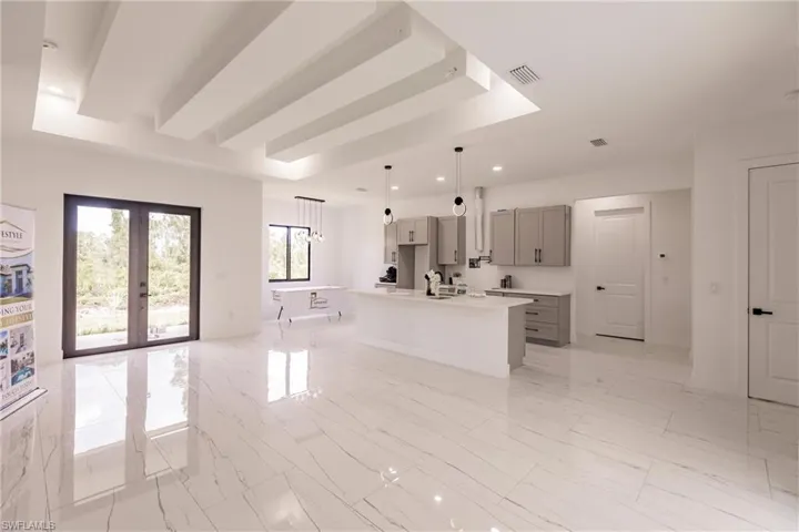 Kitchen featuring decorative light fixtures, french doors, light tile flooring, and a kitchen island with sink