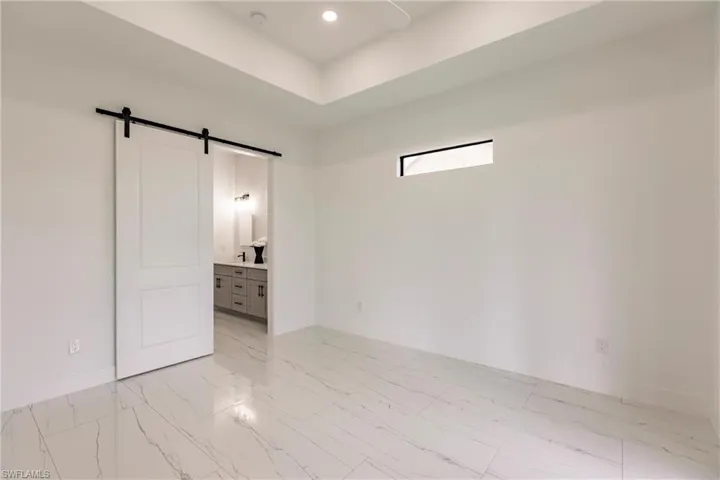 Unfurnished bedroom featuring ensuite bath, light tile floors, and a barn door