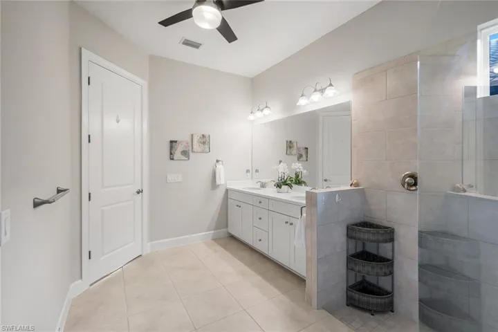 Bathroom featuring double vanity, light tile patterned floors, a ceiling fan, and walk in shower