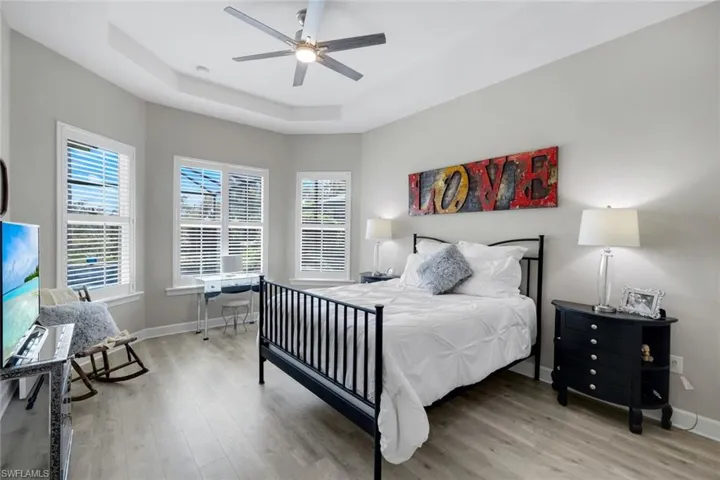 Bedroom featuring a tray ceiling, light wood-style floors, and ceiling fan