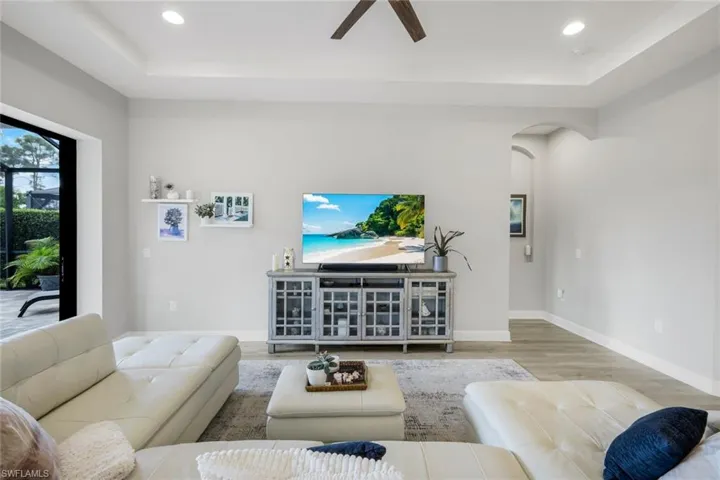 Living room featuring a raised ceiling, Luxury vinyl plank floors, arched walkways, recessed lighting, and a ceiling fan