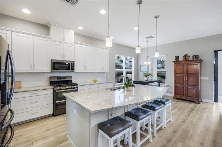 Kitchen with a extra-large quartz island, appliances with stainless steel finishes, backsplash, luxury vinyl plank flooring, pendant lights and recessed lighting