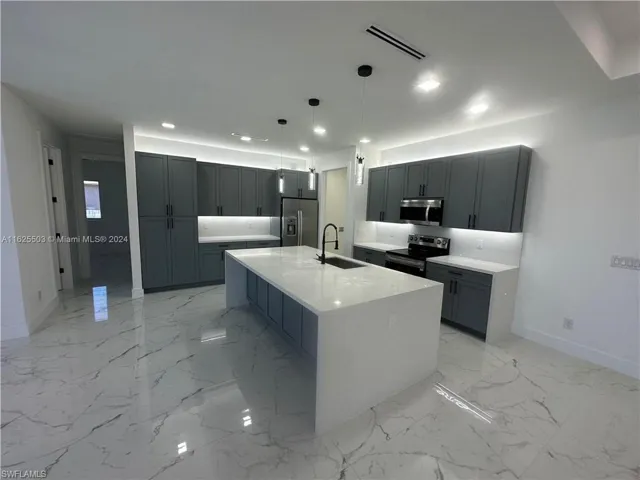 Kitchen featuring decorative backsplash, appliances with stainless steel finishes, a center island with sink, light tile patterned floors, and sink
