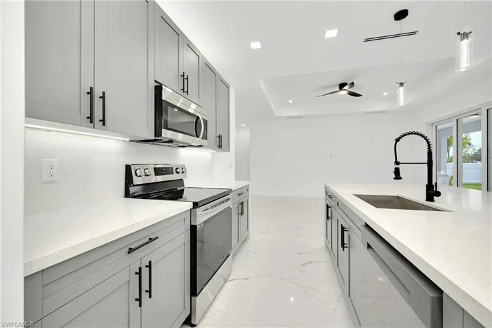 Kitchen with appliances with stainless steel finishes, ceiling fan, sink, gray cabinetry, and decorative light fixtures