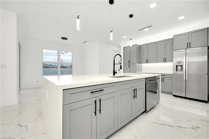 Kitchen with appliances with stainless steel finishes, an island with sink, pendant lighting, and gray cabinets