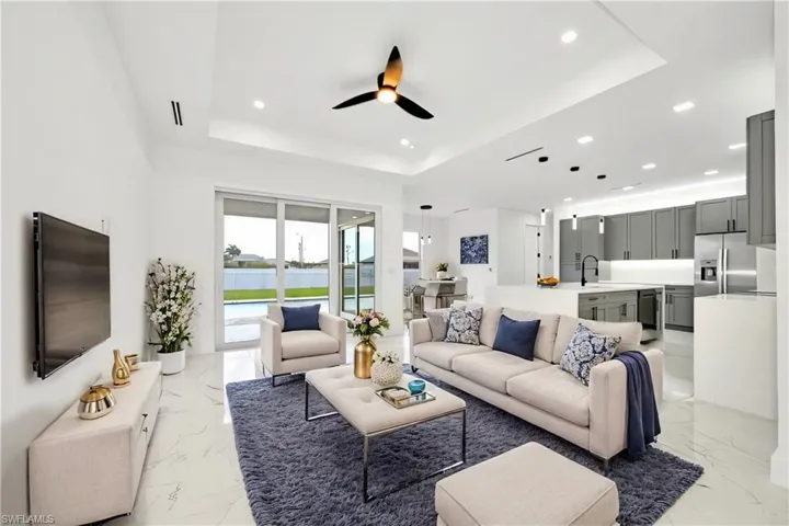 Living room with light tile patterned flooring, sink, ceiling fan, and a raised ceiling