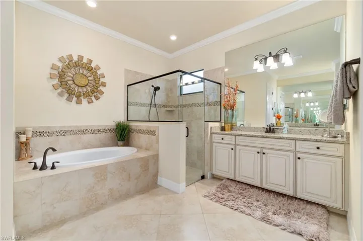 Bathroom featuring a built-in soaking tub, a frameless glass shower enclosure, a double vanity with stone-finish countertop, and tile flooring