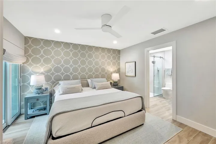 1st floor guest Bedroom with baseboards, visible vents, wallpapered walls, an accent wall, and light wood-type flooring