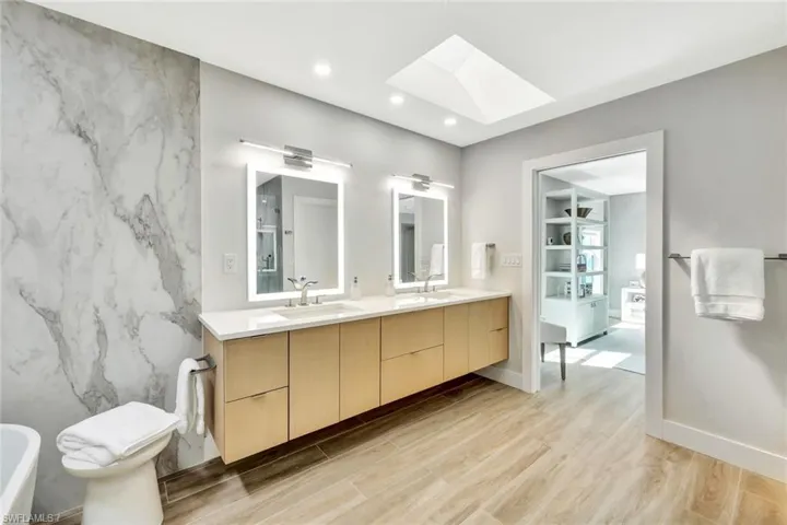Primary Full bath featuring double vanity, a skylight, wood finished floors, and a sink