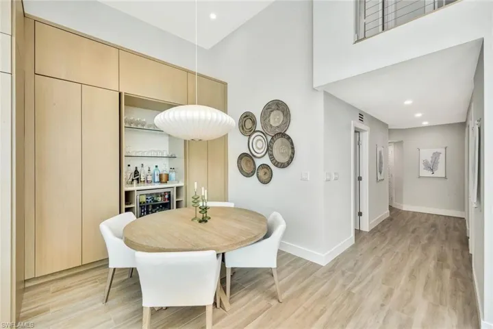 Dining area with light wood-style flooring, beverage cooler, a towering ceiling, baseboards, and a dry bar