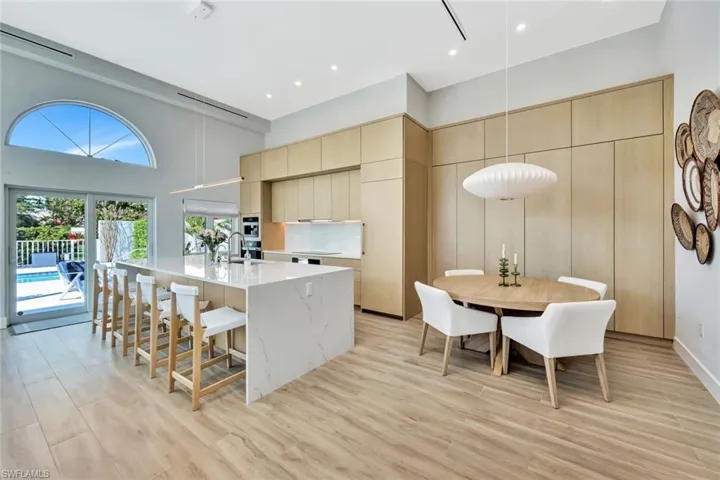 Kitchen featuring modern cabinets, a center island with sink, a sink, cream cabinets, and a towering ceiling