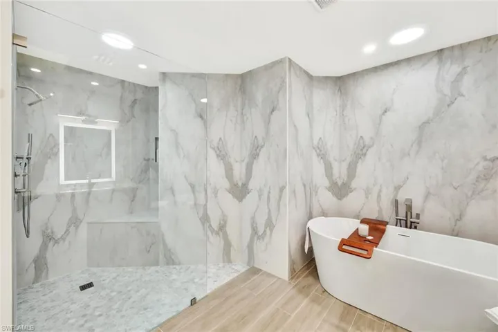 Primary bath with a marble finish shower, a soaking tub, recessed lighting, and wood finish floors