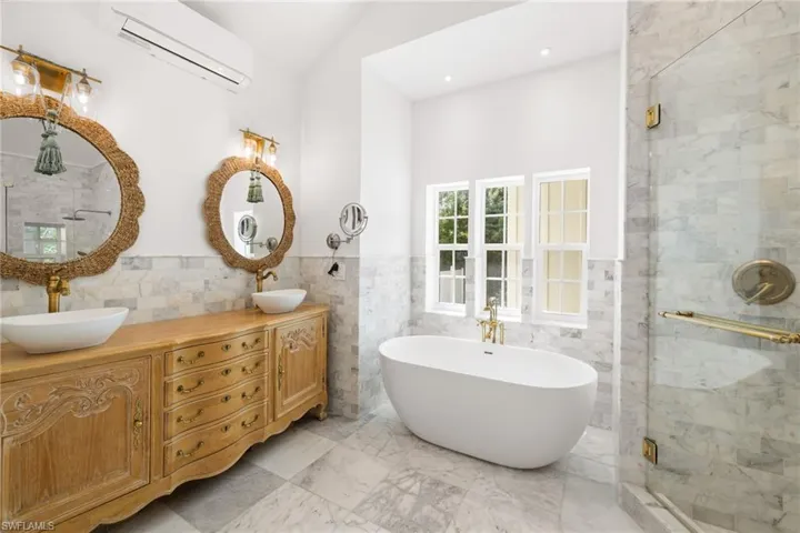 Bathroom featuring a shower stall, double vanity, a soaking tub, tile walls, and a wall unit AC