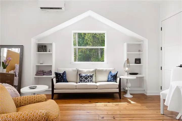 Living area with a wall unit AC, hardwood / wood-style flooring, and lofted ceiling