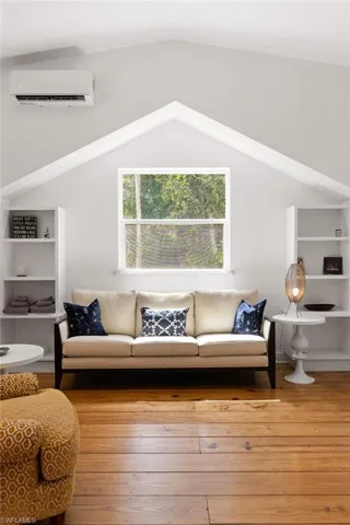 Living room featuring vaulted ceiling, hardwood / wood-style floors, and an AC wall unit