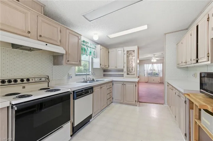Kitchen with white appliances, light flooring, light countertops, wallpapered walls, and a textured ceiling