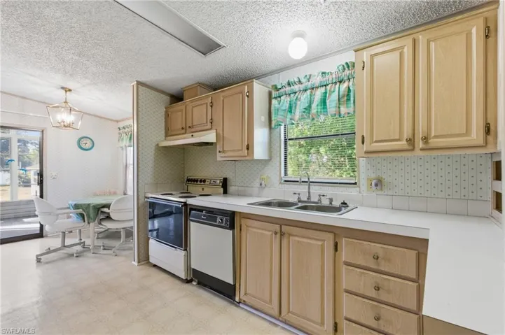 Kitchen with light wood finish cabinets, light countertops, wallpapered walls, light flooring, and white appliances