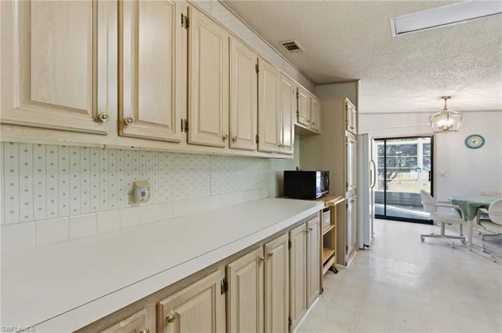 Kitchen featuring wallpapered walls, light flooring, light countertops, light wood finish cabinetry, and black microwave