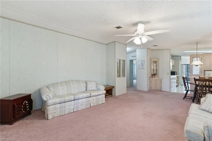 Living room featuring carpet, a ceiling fan, and a textured ceiling