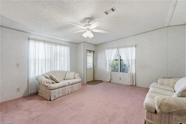 Carpeted living area featuring ceiling fan, ornamental molding, and a textured ceiling