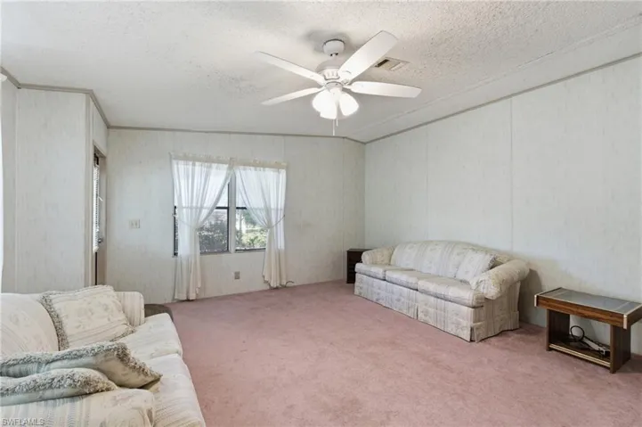 Living room featuring carpet flooring, a ceiling fan, a textured ceiling, and crown molding