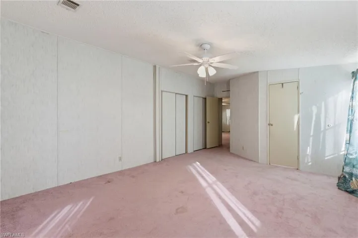 Unfurnished bedroom with two closets, a textured ceiling, carpet, and a ceiling fan