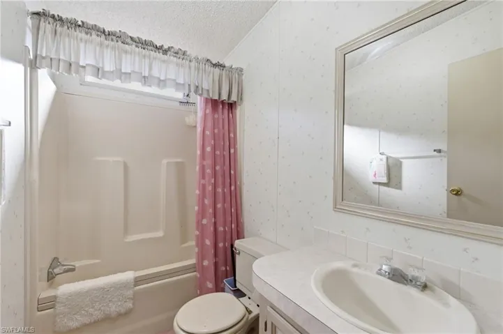 Full bath with shower / bath combination with curtain, vanity, a textured ceiling, and wallpapered walls