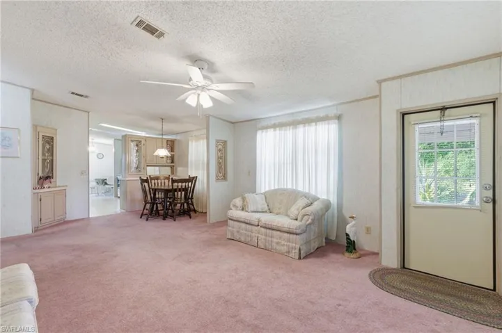 Living room with ceiling fan, light colored carpet, ornamental molding, and a textured ceiling