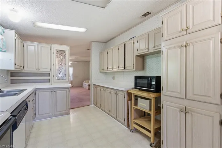 Kitchen featuring light floors, a textured ceiling, light countertops, wallpapered walls, and black microwave