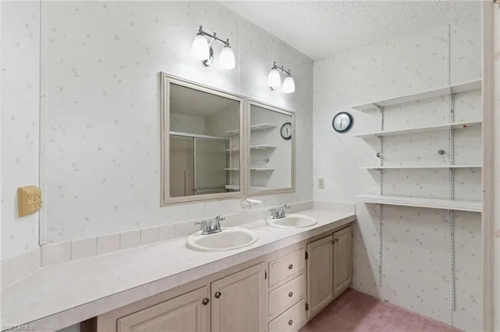 Bathroom featuring wallpapered walls, a shower stall, double vanity, and a textured ceiling