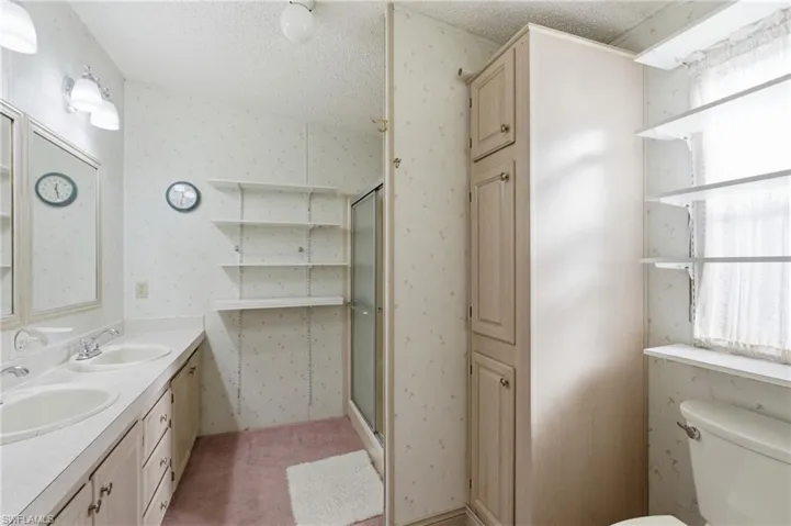 Bathroom with wallpapered walls, a textured ceiling, a shower stall, double vanity, and plenty of natural light