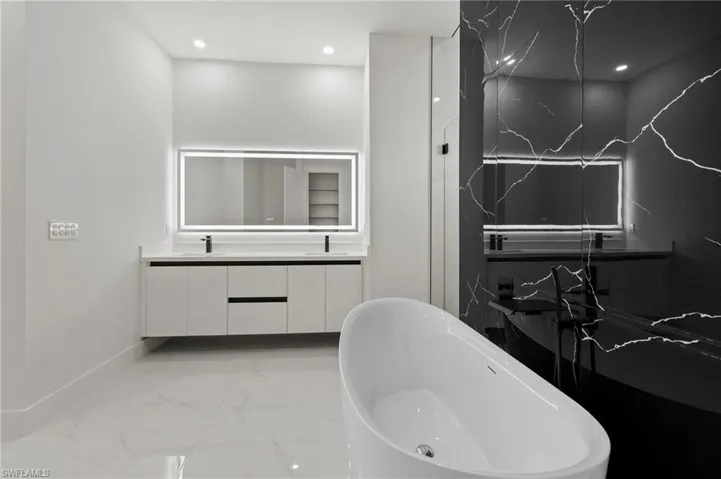 Full bathroom featuring double vanity, a soaking tub, recessed lighting, marble finish floor, and a sink