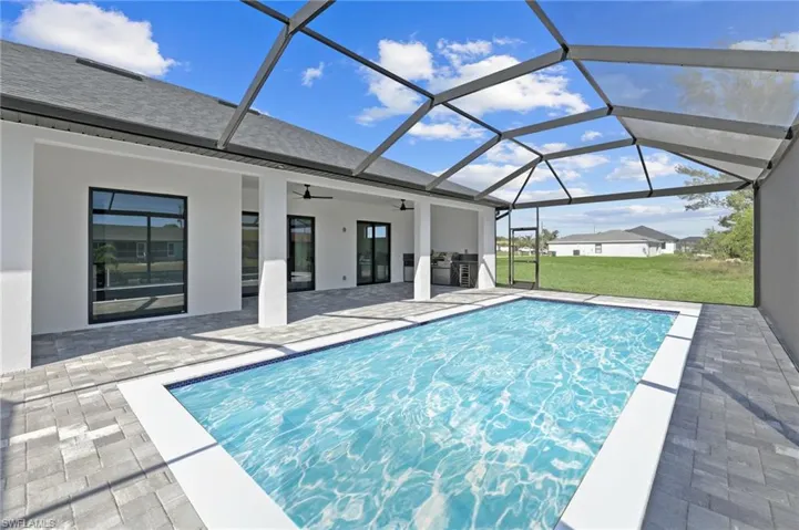 View of swimming pool featuring a ceiling fan, a lawn, a patio area, exterior kitchen, and a lanai