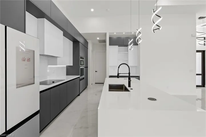 Kitchen with black electric stovetop, freestanding refrigerator, modern cabinets, marble finish floor, and a sink
