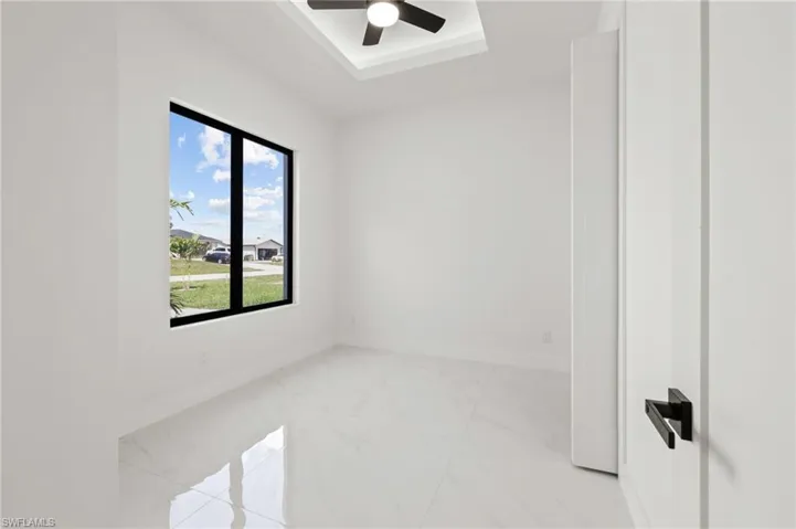Unfurnished room featuring a tray ceiling, marble finish floor, baseboards, and a ceiling fan