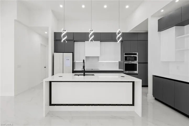 Kitchen with freestanding refrigerator, modern cabinets, double oven, marble finish floor, and a sink