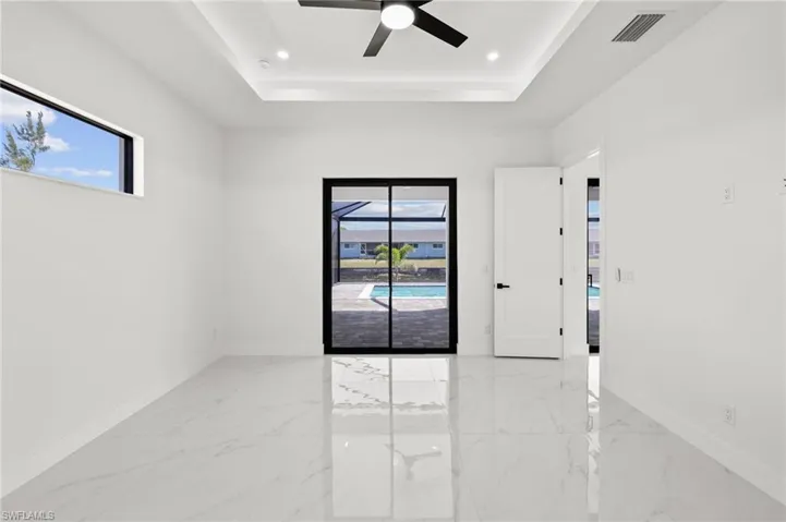 Empty room featuring a raised ceiling, marble finish floor, ceiling fan, and baseboards