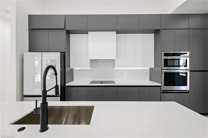 Kitchen with custom exhaust hood, black electric cooktop, a sink, double oven, and gray cabinets