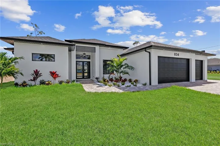 Prairie-style home with a garage, a front yard, stucco siding, and french doors