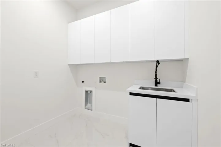 Clothes washing area with a sink, hookup for an electric dryer, cabinet space, marble finish floor, and hookup for a washing machine