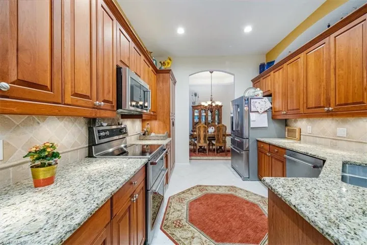 Kitchen with stainless steel appliances, light stone countertops, light tile patterned flooring, an inviting chandelier, and tasteful backsplash