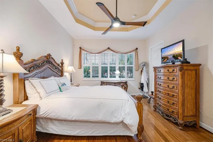 Bedroom with ornamental molding, hardwood / wood-style floors, a raised ceiling, and ceiling fan