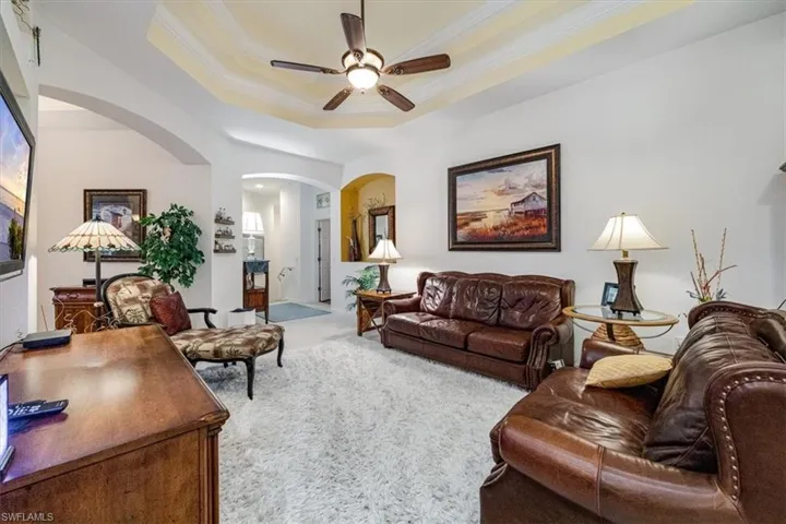 Living room with crown molding, a tray ceiling, carpet floors, and ceiling fan